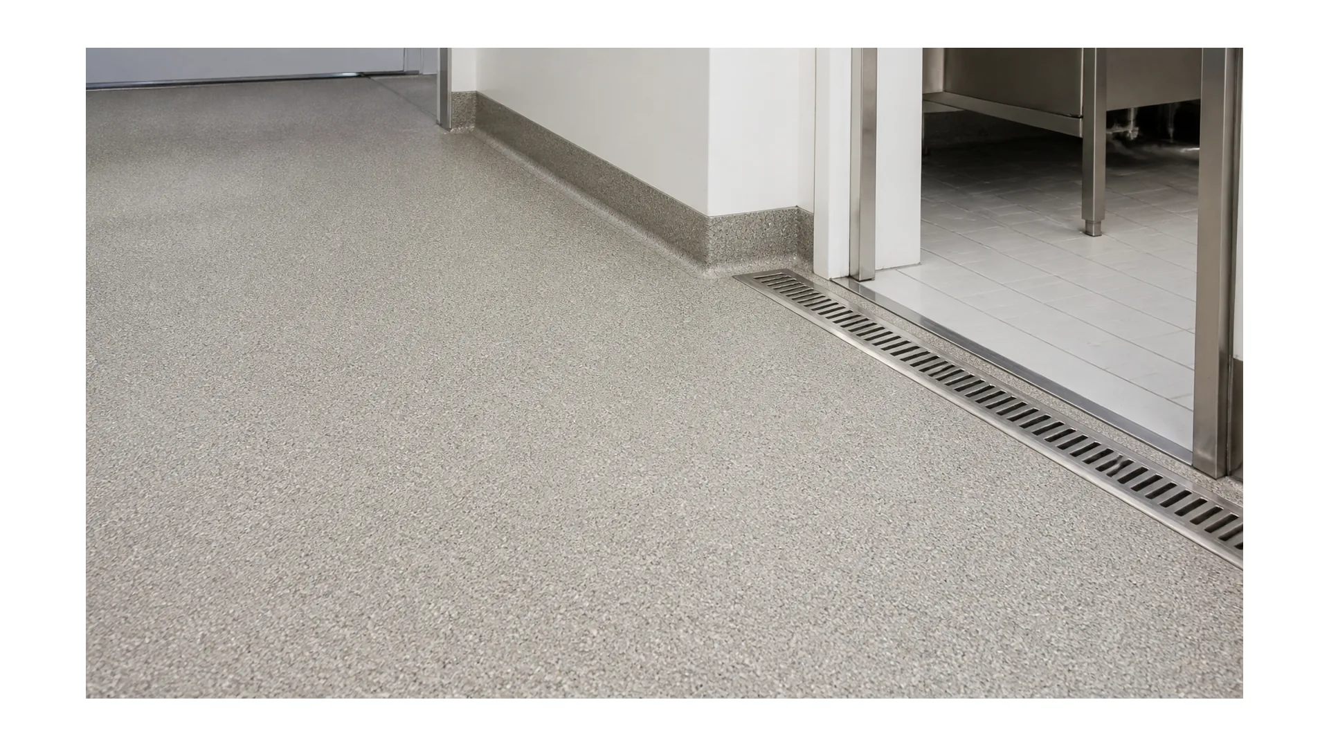 Textured non-slip resinous flooring with drain and transition detail in a wet-area corridor